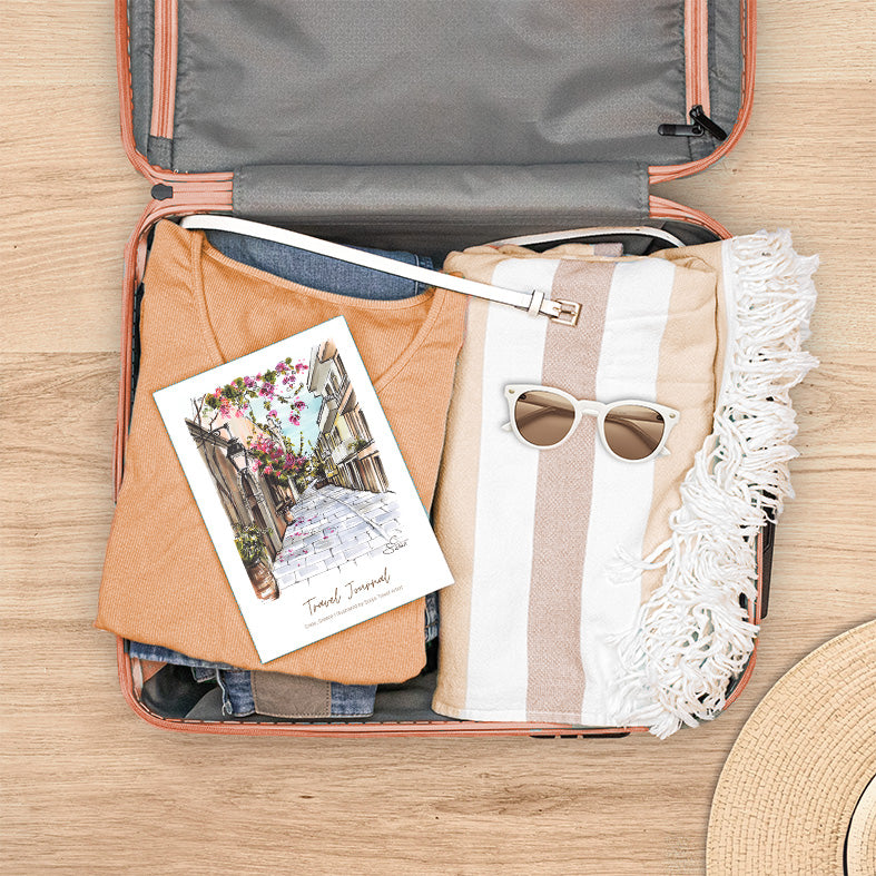 Reisetagebuch Griechenland mit handgezeichneter Illustration einer griechischen Straße mit Bougainvillea,  bereit für die Reise im Koffer
